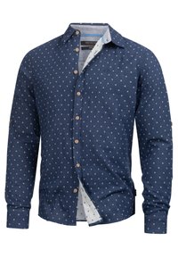 Camisa de manga larga azul marino con patrón geométrico blanco, interior del cuello en contraste y botones de madera. Tejido ligero y corte relajado.