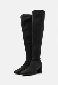 Botas negras hasta la rodilla de tejido suave, con puntera cuadrada y tacón cuadrado. Diseño limpio con detalles de costuras mínimas.
