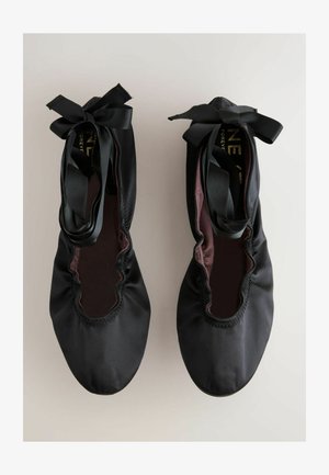 Schwarze Ballerinas aus glattem Satin, mit einem gerafften Rand, runder Zehenform und langen Satinschleifen, die um den Knöchel gebunden sind.