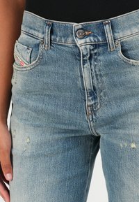 Light blue denim jeans with a faded finish, five pockets, and a button closure. Features stitching accents and slight wear near pockets.