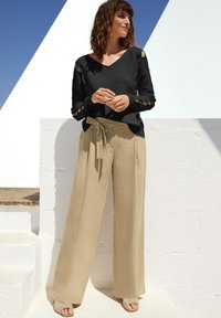 Schwarzer V-Ausschnitt-Pullover mit Ausschnittdetails an den Ärmeln, kombiniert mit hoch taillierten beigen, weiten Hosen, die an der Taille gebunden sind, und hellen Sandalen.