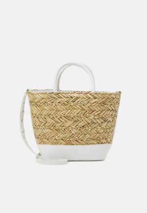 Sac fourre-tout en paille tissée avec base en cuir blanc, poignées courtes et bandoulière réglable, posé sur un fond uni.