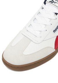 Baltas odinis ir zomšinis sportbačiai su raudonomis detalėmis, guminis padas ir baltos raišteliai. Išskirtas švarus dizainas su kontrastuojančiomis lygiomis ir tekstūruotomis paviršiais.