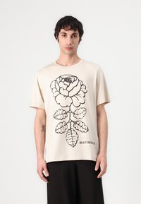 Beige bomull T-skjorte med et stort svart blomstermønster med en rose og blader. Løs passform og kortermer, merket "marimekko."