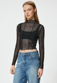 Crop top noir transparent à manches longues avec des d�étails texturés et un col haut, associé à un jean en denim bleu clair taille haute.