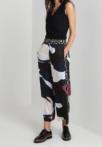 Top nero avvolgente abbinato a pantaloni larghi con motivo nei colori nero, blu navy, bordeaux e crema. I pantaloni presentano una vita elasticizzata e tasche.