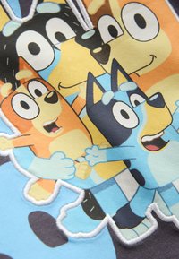 Quatre personnages de chiens animés aux couleurs vives souriant et se tenant la main sur un fond en tissu bleu clair.