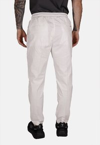 Pantalones ligeros beige con una cinturilla elástica, dos bolsillos traseros y un diseño de pierna ajustada. Llevados con zapatillas negras.