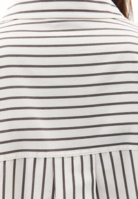 Gestreifte Bluse in Weiß und Dunkelbraun, mit klassischem Kragen und Falten-Detail auf der Rückseite. Glattes Material mit gleichmäßiger Textur.