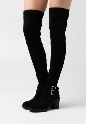 Botas negras por encima de la rodilla en suave ante, con un tacón grueso, acentos de doble hebilla y un cierre lateral para facilitar el uso.