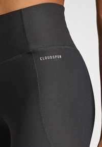 Schwarze High-Waist-Leggings aus einem glatten, dehnbaren Stoff. Bemerkenswerte Nähte und das "CLOUDSPUN"-Logo in Weiß auf dem Bund.