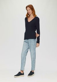 Marineblaues V-Neck-Pullover mit gerippter Textur, kombiniert mit hellblauen Jeans und schwarzen Sneakers mit strukturiertem Sohlen und hellen Akzenten.