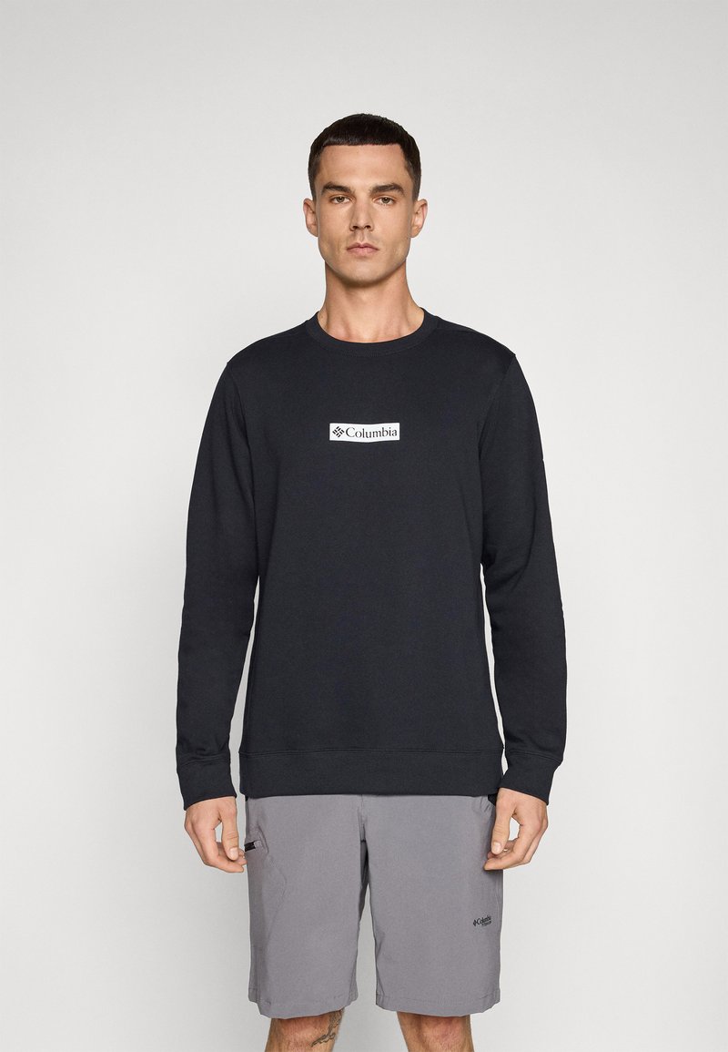Sweatshirt noir à manches longues et col rond. Présente un logo "Columbia" blanc sur la poitrine. Le tissu semble doux avec une coupe standard.