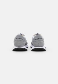 Zapatillas deportivas grises con parte superior de ante y malla, tacón redondeado, logotipo icónico en la parte trasera y una media suela blanca en contraste.