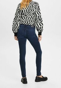 Vaqueros ajustados de color azul oscuro con una textura suave y detalles mínimos, combinados con un suéter negro y blanco con estampado. Zapatos negros con suelas gruesas.