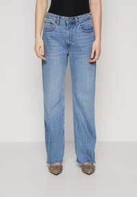 Light blue straight-leg jeans feature a classic five-pocket design, mid-rise waist, and subtle fading. Paired with beige pointed-toe flats.