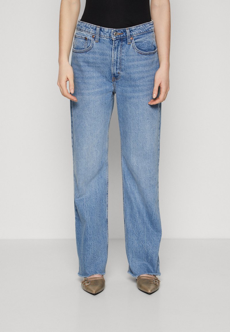 Light blue straight-leg jeans feature a classic five-pocket design, mid-rise waist, and subtle fading. Paired with beige pointed-toe flats.