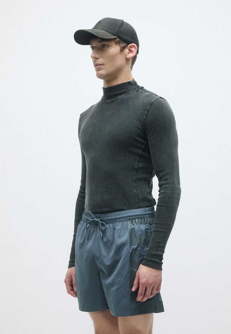 Donkergrijze lange mouw ribshirt gecombineerd met lichtblauwe shorts. De outfit bevat een zwarte pet, wat de sportieve uitstraling benadrukt.