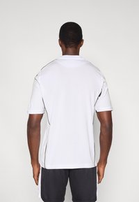 Hvid polo-shirt med korte ærmer, med sort piping langs skuldrene og siderne. Letvægts, åndbart stof, enkelt design.