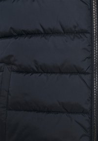 Puffer jacket in dark navy blue, featuring a quilted pattern with horizontal sections, a zippered front, and a smooth, soft texture.
