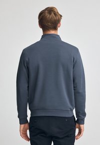 Mörkgrå sweatshirt med hög krage, ribbade ärmslut och midja. Slät textur, minimalistisk design och inga synliga logotyper eller mönster.