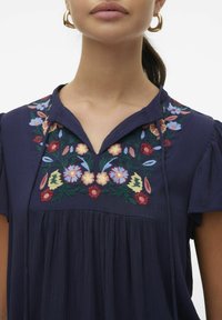 Blusa blu navy a maniche corte con un design plissè e un vivace ricamo floreale sul colletto in rosa, giallo, blu e verde.