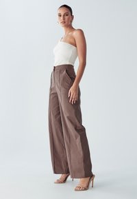 Brązowe spodnie z wysokim stanem, z plisami, oraz dopasowany biały prążkowany top. Dopełnieniem stroju są sandały na wysokim obcasie w kolorze piaskowym.