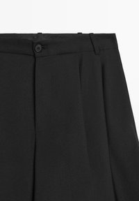 Schwarze Hose mit flacher Vorderseite, seitlichen Falten, Taillenknaopf und Gürtelschlaufen. Hergestellt aus strukturiertem Stoff mit einem klaren, maßgeschneiderten Design.