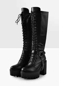 Black leather knee-high boots with lace-up front, chunky platform and heel, side chain accent, and contrasting smooth and textured finishes.