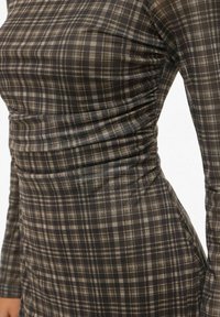 Robe ajustée avec un motif écossais marron et crème, présentant des détails froncés sur les côtés et des manches longues. Confectionnée dans un tissu lisse et extensible.