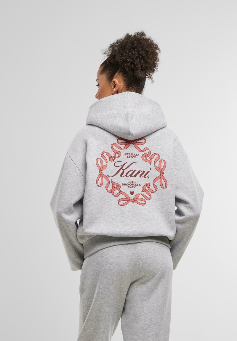 Sivý mikina s kapucňou, ktorá má okrúhly potlač s červenými stuhami a nápisom "Spread Love" a "Kani, The Brooklyn Way" na chrbte.