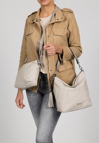 Sacs à bandoulière gris clair en tissu doux, avec des accents argentés et un détail pompon, assortis à une veste kaki et un jean gris.