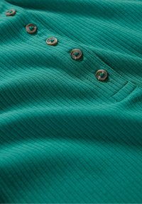 Zeleni rebrasti materijal s pet smešnih dugmadi sa jedne strane i vidljivom džepom, koji prikazuje meku teksturu.