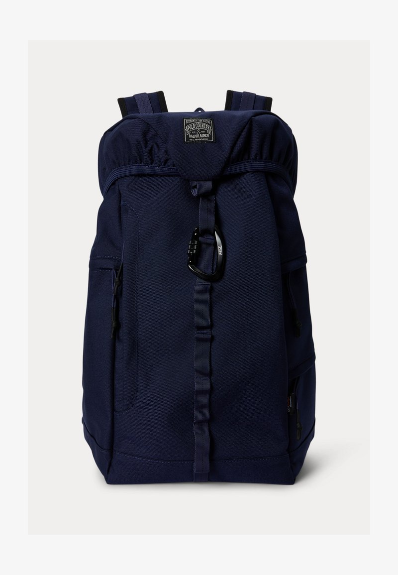 Σακίδιο πλάτης σκούρου μπλε χρώματος με επάνω καπάκι, ρυθμιζόμενους ιμάντες ώμου, μπροστινή θηλιά με μαύρο καραμπίνερ και λογότυπο στο κέντρο του επάνω μέρους.