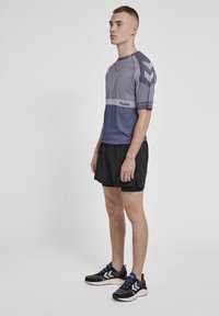 Kortebloemige paarse en grijze sportshirt met verticale strepen, gecombineerd met zwarte shorts en zwarte sneakers met witte accenten.