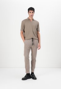 Beige short-sleeve polo with a V-neck and a textured knit. Paired with light beige tapered pants and black slip-on shoes.