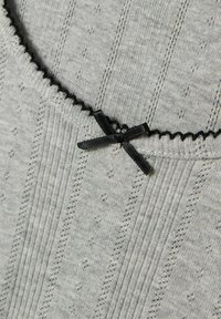 Hellgrauer gerippter Stoff mit kleinen vertikalen Mustern, gewelltem schwarzen Saum und einem kleinen schwarzen Schleifendetail nahe dem Rand.