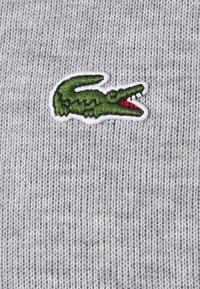 Gray knitted fabric featuring a green, embroidered crocodile logo with red accents on a white border.