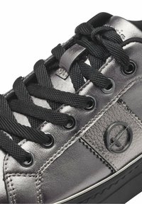 Metallisch grauer Sneaker mit dicken schwarzen Schnürsenkeln, dekorativem strukturiertem Einsatz, schwarzem runden Logo und schwarzer Gummisohle.