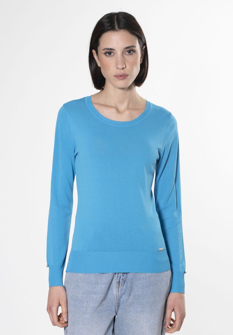 Maglione azzurro chiaro a maniche lunghe con scollatura rotonda e orlo a costine. Presenta maniche aderenti e un piccolo accento metallico nella parte inferiore.