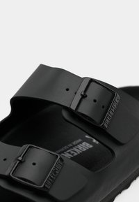 Sandale Birkenstock noire avec deux sangles réglables à boucle et un semelle en relief sur fond blanc.