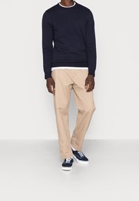 Marinblå stickad tröja med strukturerat mönster, beige byxor och marinblå sneakers med vita sulor. Inga synliga mönster eller detaljer på byxorna.