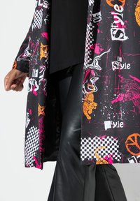Túnica larga y estampada con base negra, que presenta diseños gráficos en tonos rosa brillante, naranja y blanco, así como cuadros y motivos animales; combinada con pantalones negros.