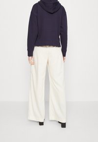 Sudadera con capucha de color azul marino y un diseño recortado, combinada con unos pantalones de pierna ancha en color crema con rayas. Los pantalones presentan un tejido suave y texturizado.