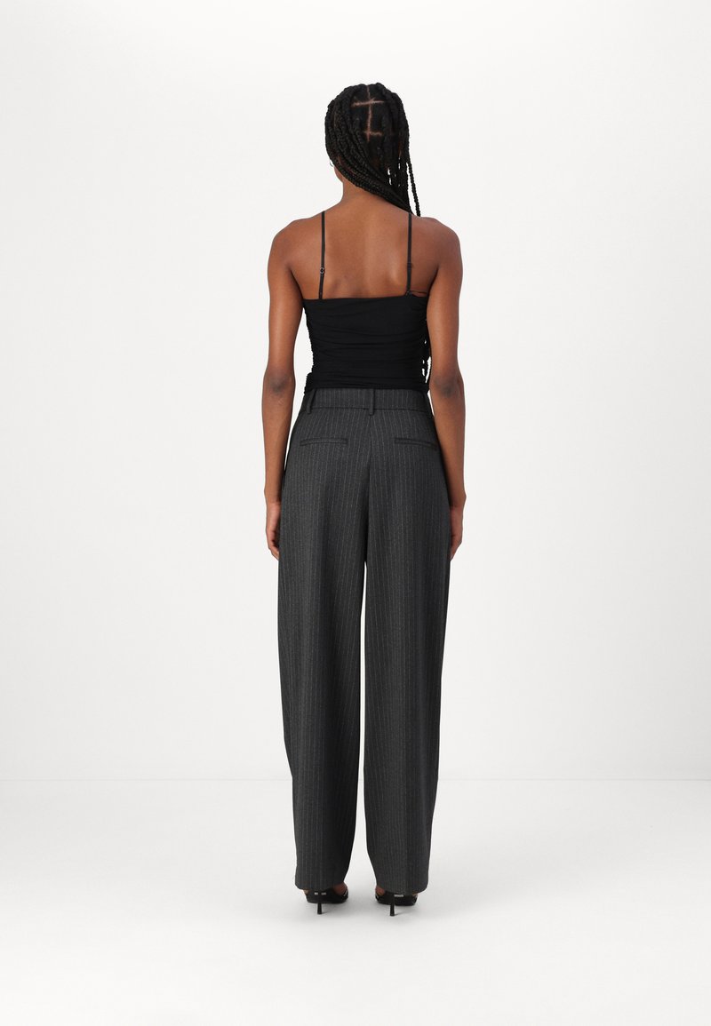 Schwarzes gerafftes Camisole-Top kombiniert mit hoch taillierten, weit geschnittenen, grauen gestreiften Hosen mit Gesäßtaschen und glatter Textur.