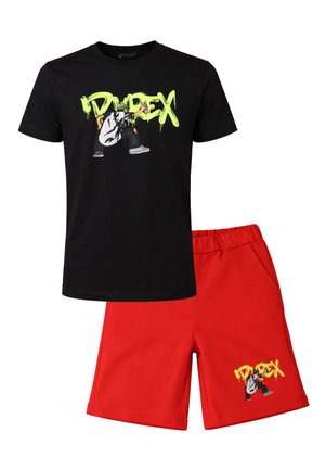 Maglietta nera con scritta graffiti verde neon e figura accovacciata, abbinata a pantaloncini rossi con la stessa grafica sulla gamba.