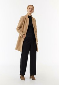Beige Wollmischungs-Mantel mit strukturiertem Design, schwarzem geripptem Rollkragenpullover, weiten schwarzen Hosen und tannfarbenen hochhackigen Stiefeletten.