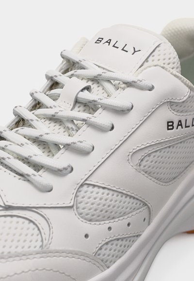 Baskets blanches Bally avec panneaux en maille, lacets blancs et texte du logo sur la languette et le côté, présentées en vue rapprochée et en angle.