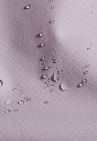 Wassertropfen perlen auf glattem, hellviolettem Stoff und heben dessen wasserabweisende Textur und gitterartiges Muster hervor.