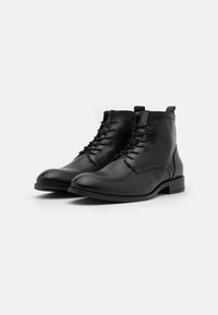 Botas de cuero negras hasta el tobillo con punta redondeada, cordones en la parte frontal y tacón pequeño. Textura suave con sutiles detalles de costura.
